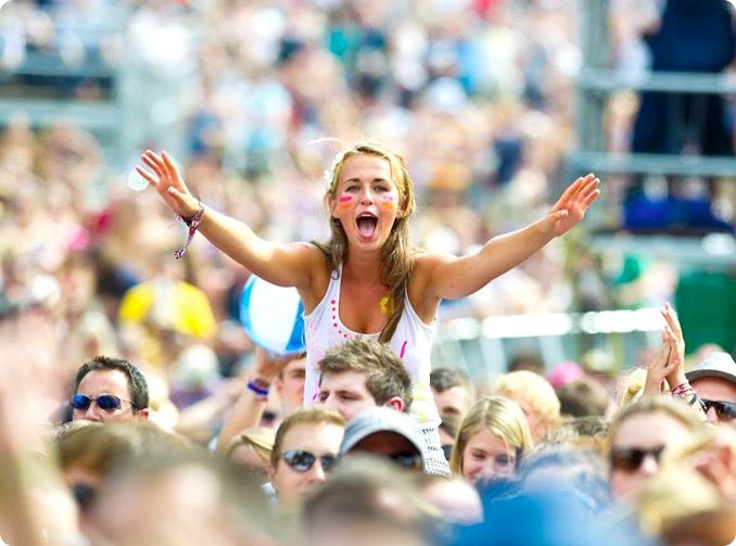 a festival scene with a person wearing a wristband & screaming while on the shoulders of a fellow event attendee 